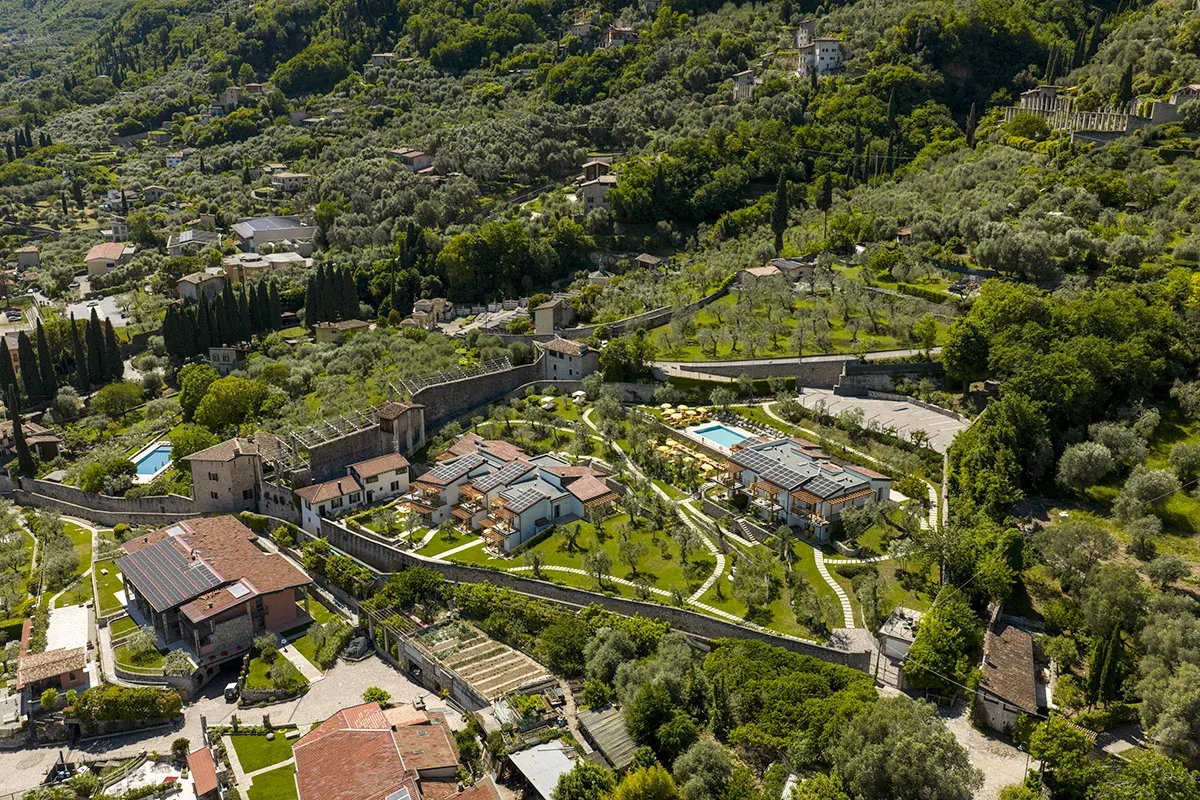 Aerial view of hillside village with olive groves, stone walls, gardens and a pool