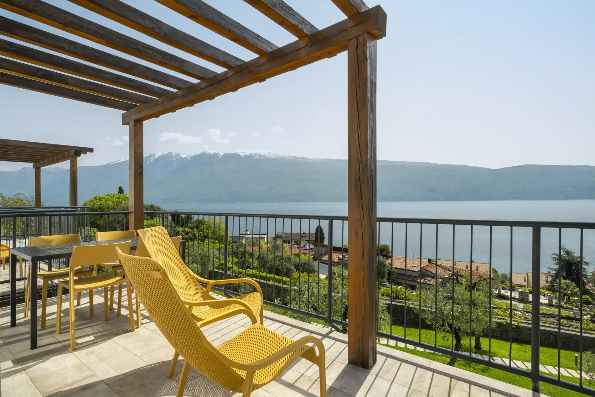Balcony with pergola and yellow chairs overlooking lake and mountains.