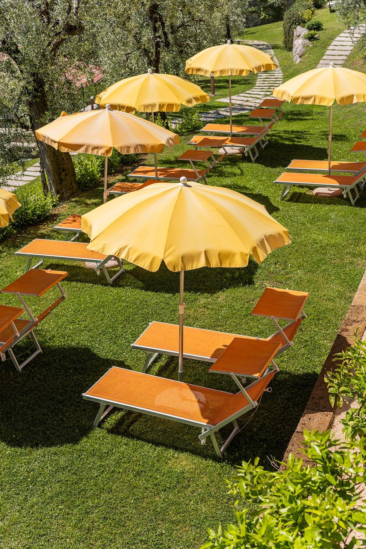 Giardino con ombrelloni gialli e lettini prendisole tra ulivi