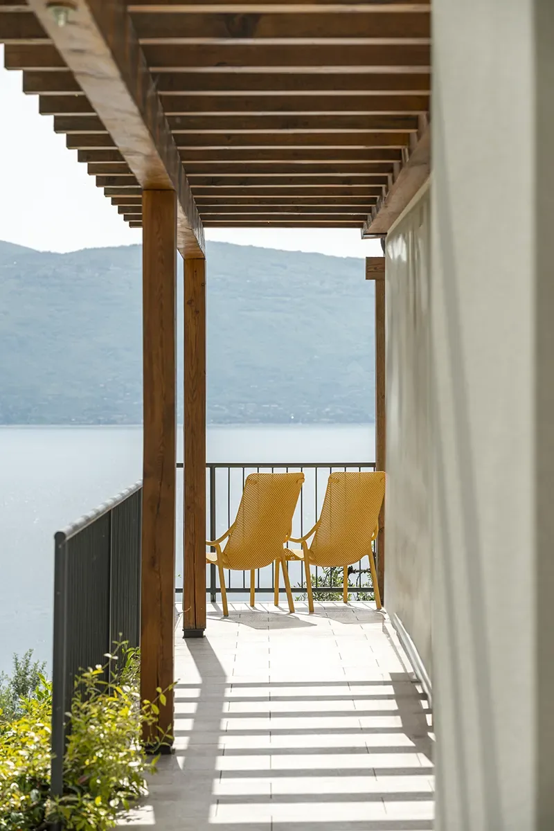 Lakeside balcony with wooden pergola and two yellow chairs overlooking mountains