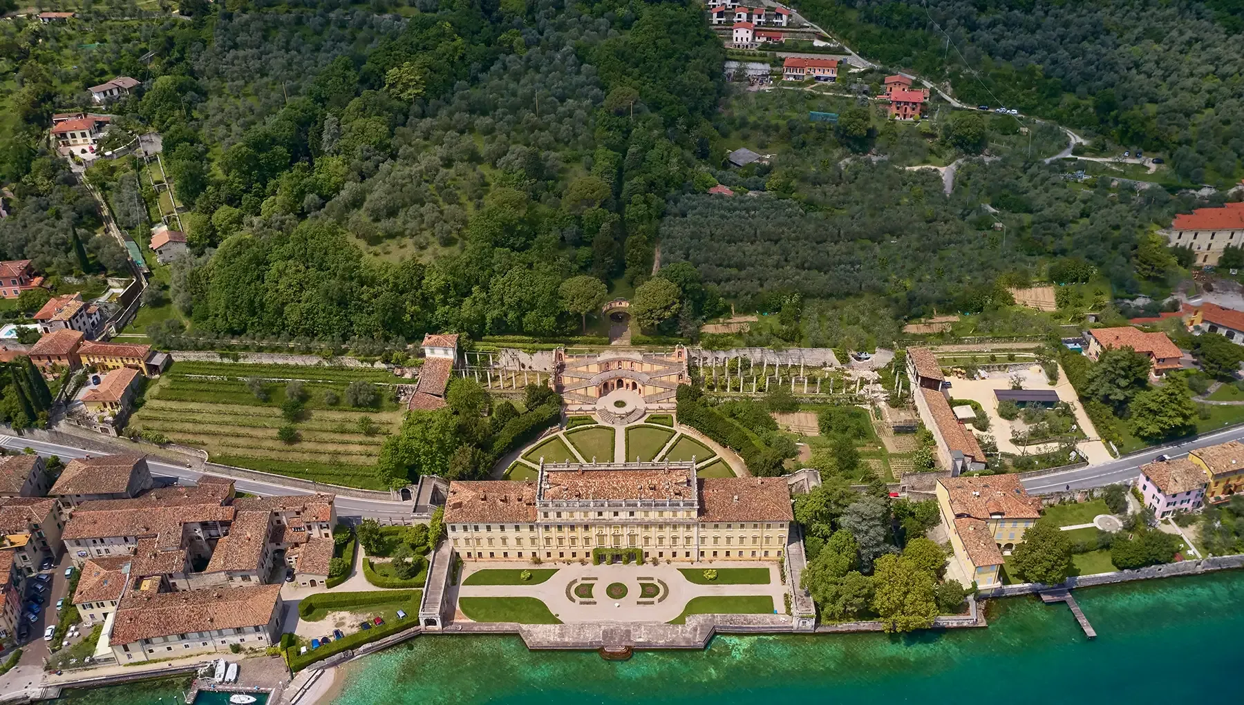 Aerial view of a lakeside historic villa with formal gardens and terraces.