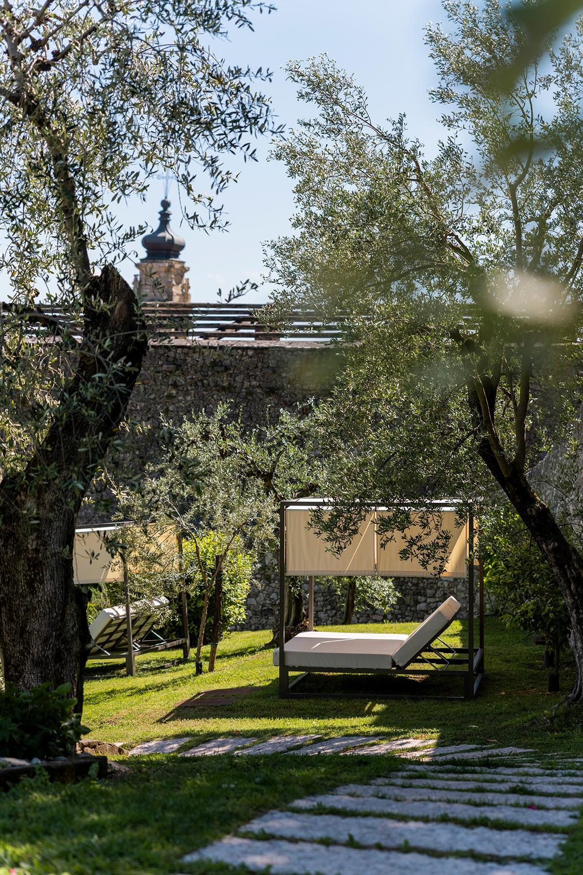 Lettino con baldacchino tra ulivi in giardino con sentiero in pietra