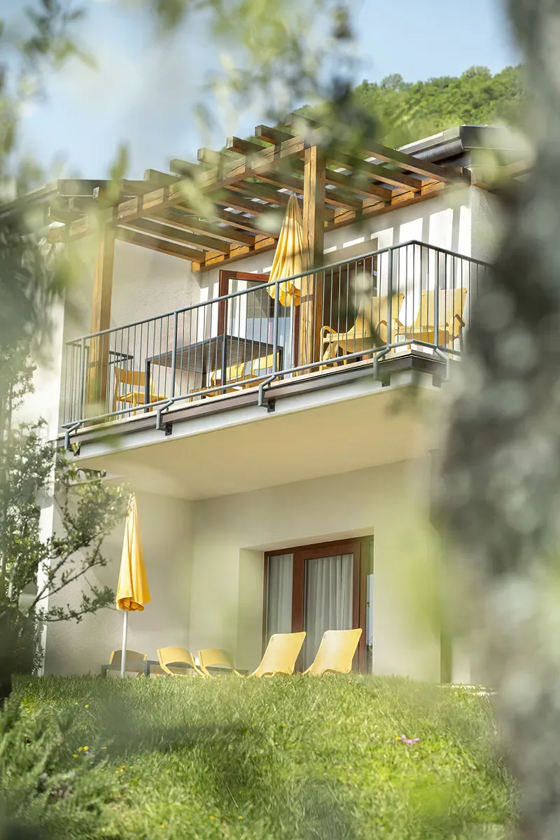 Modern house balcony with pergola, yellow chairs and umbrellas in a green garden