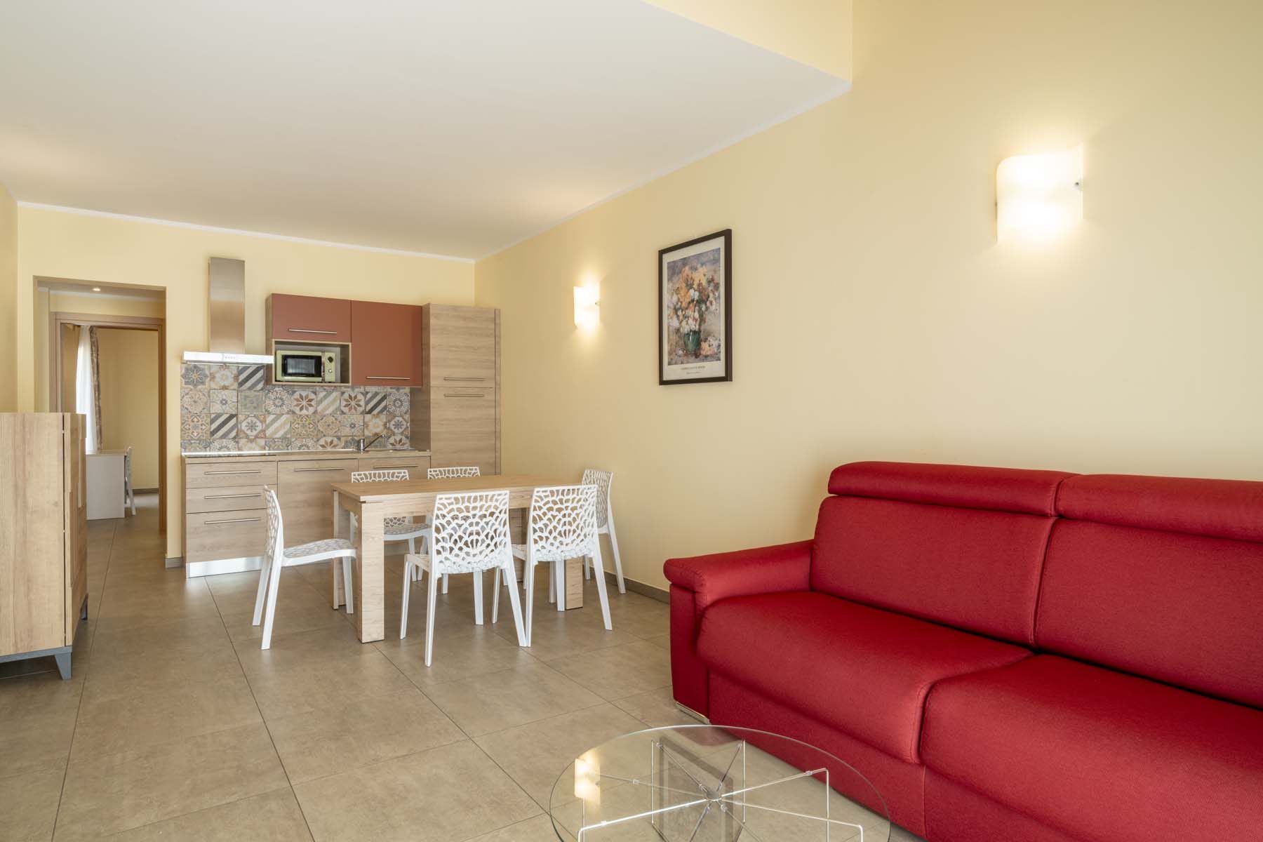 Modern apartment living room with red sofa, dining table and tiled kitchenette
