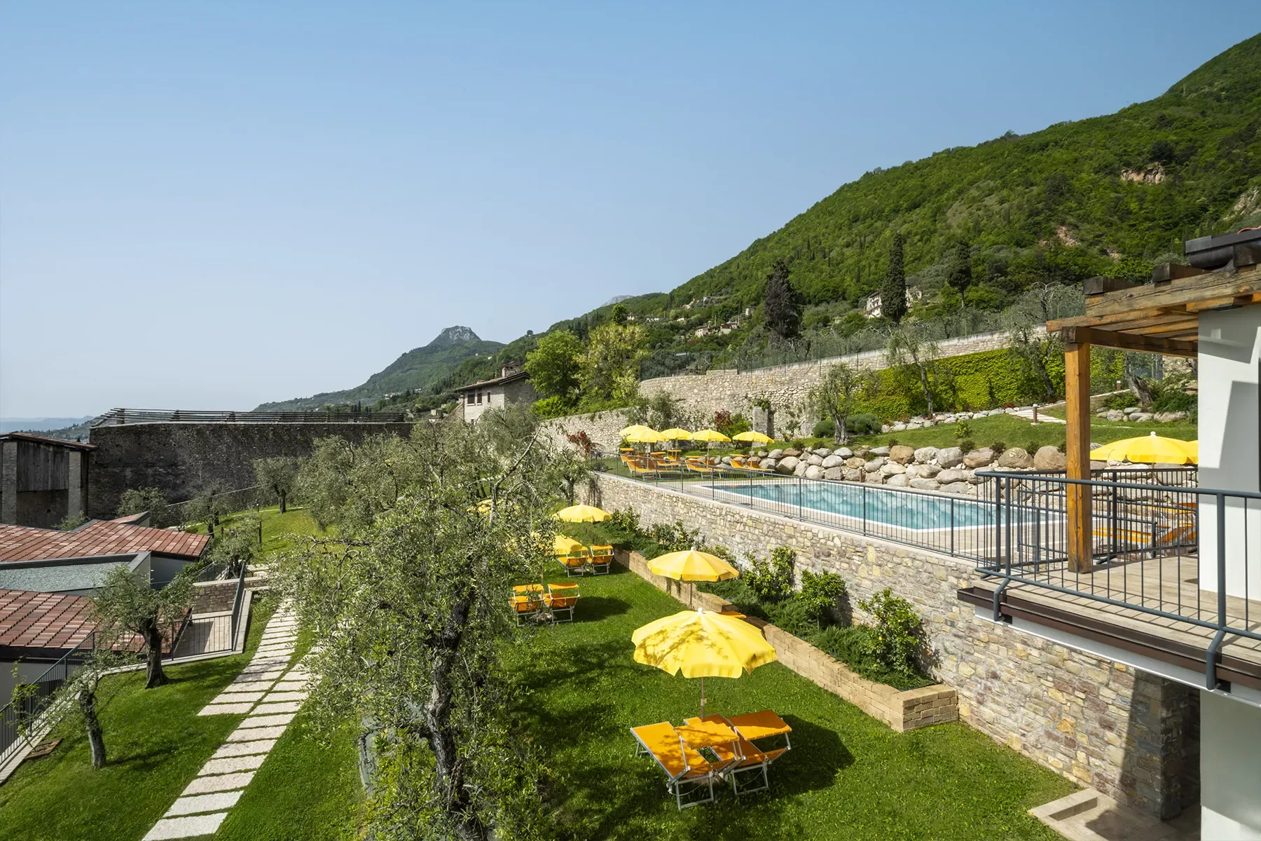Piscina panoramica con ombrelloni gialli in giardino collinare, vista sulle montagne