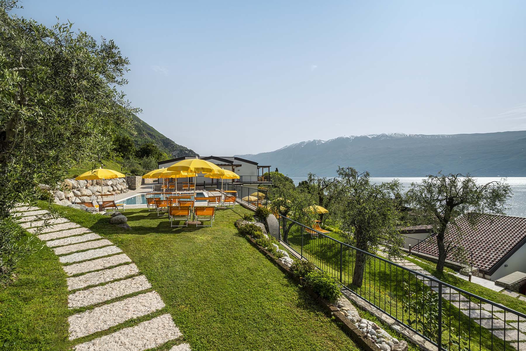 Piscina con lettini e ombrelloni gialli, vista lago e montagne.
