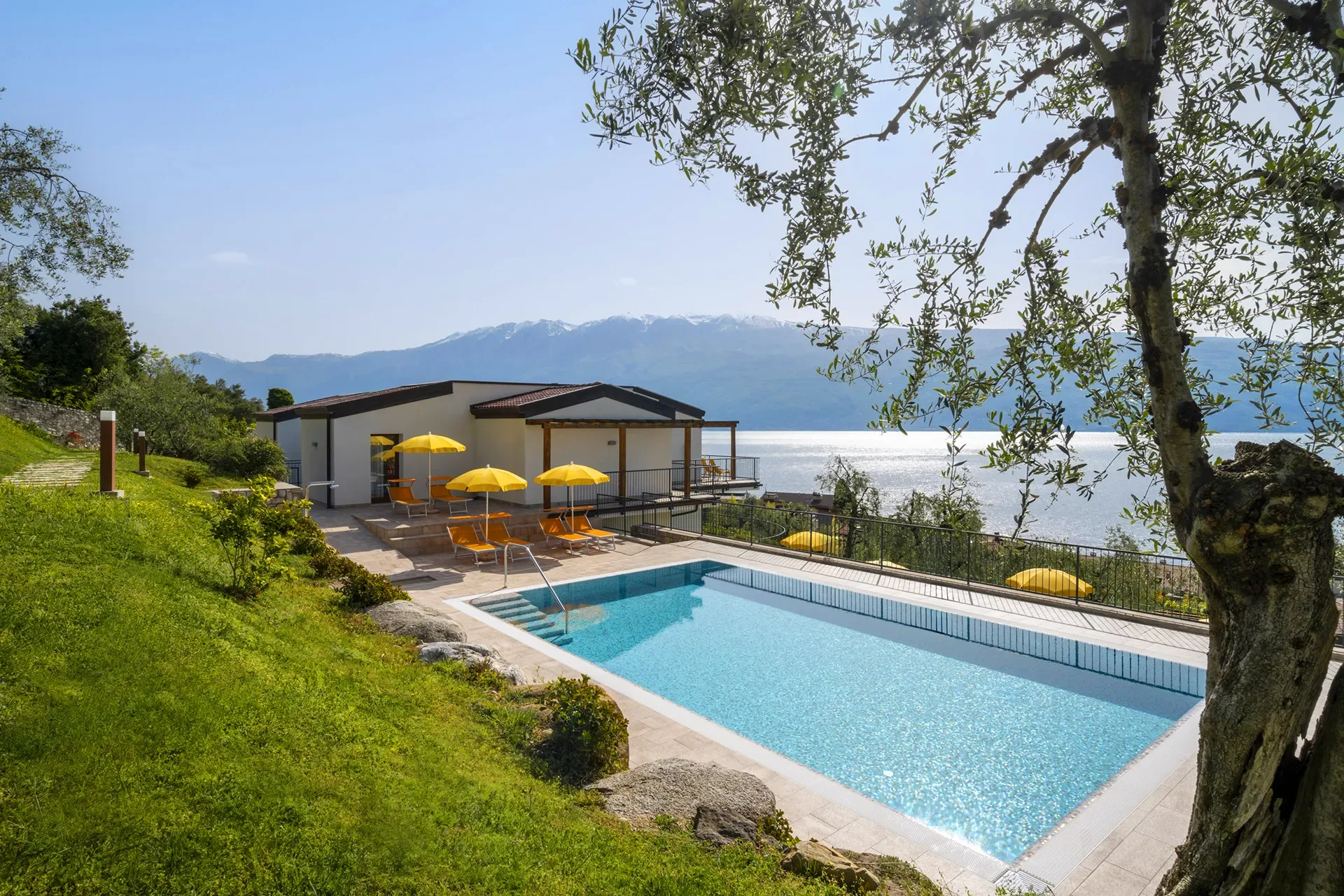 Piscina all'aperto con lettini gialli e vista lago e montagne.