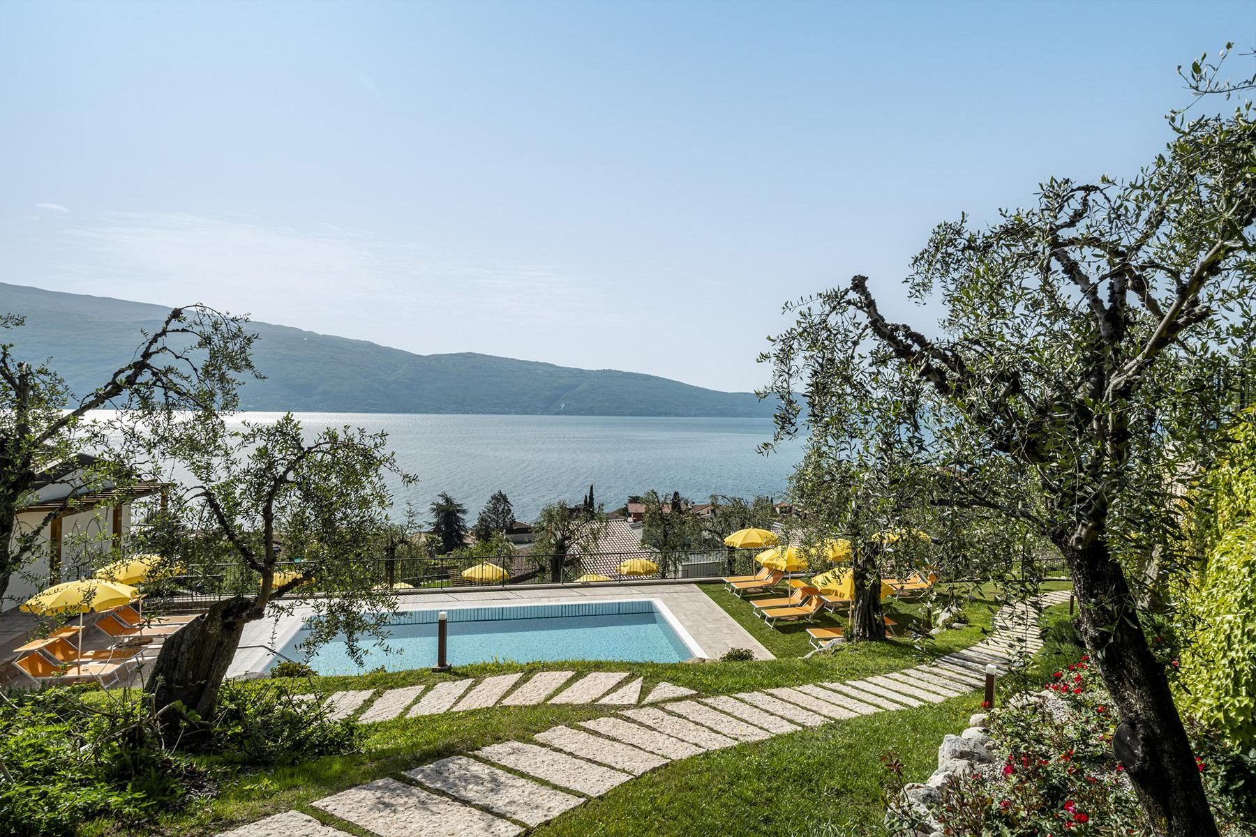 Pool mit gelben Liegen zwischen Olivenbäumen, Seeblick und Bergpanorama.